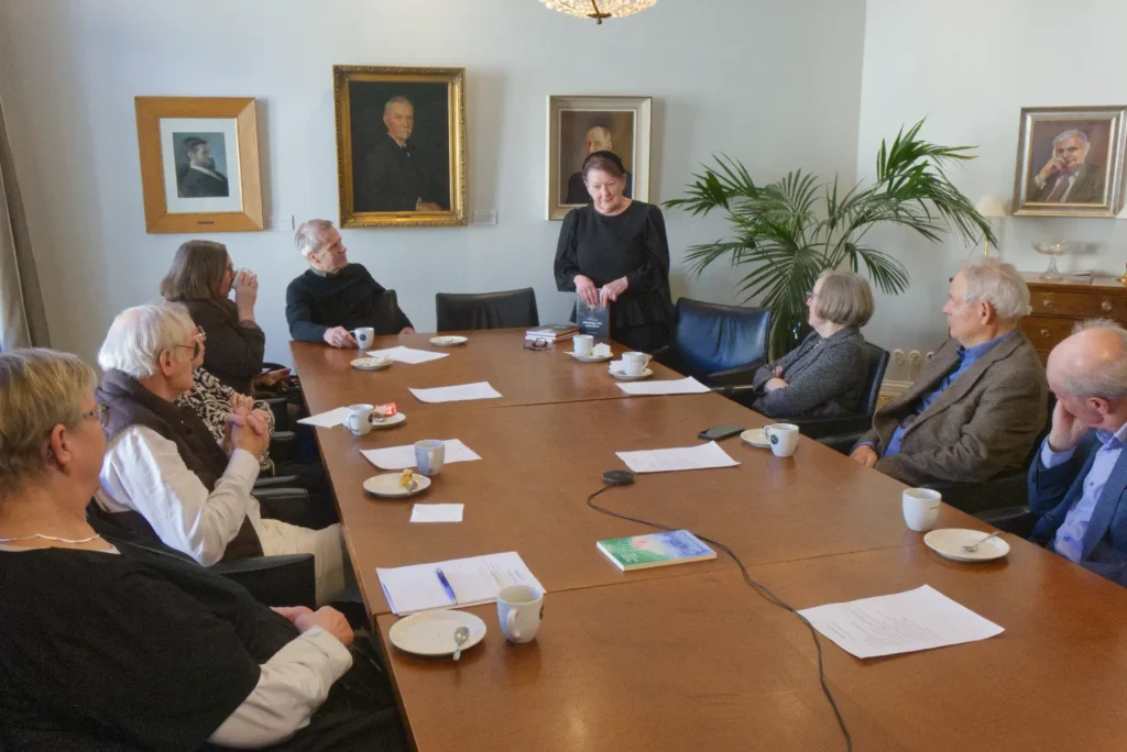 Elisabeth Sandelin berättar om sina böcker. Publiken sitter längs ett långt styrelsebord.